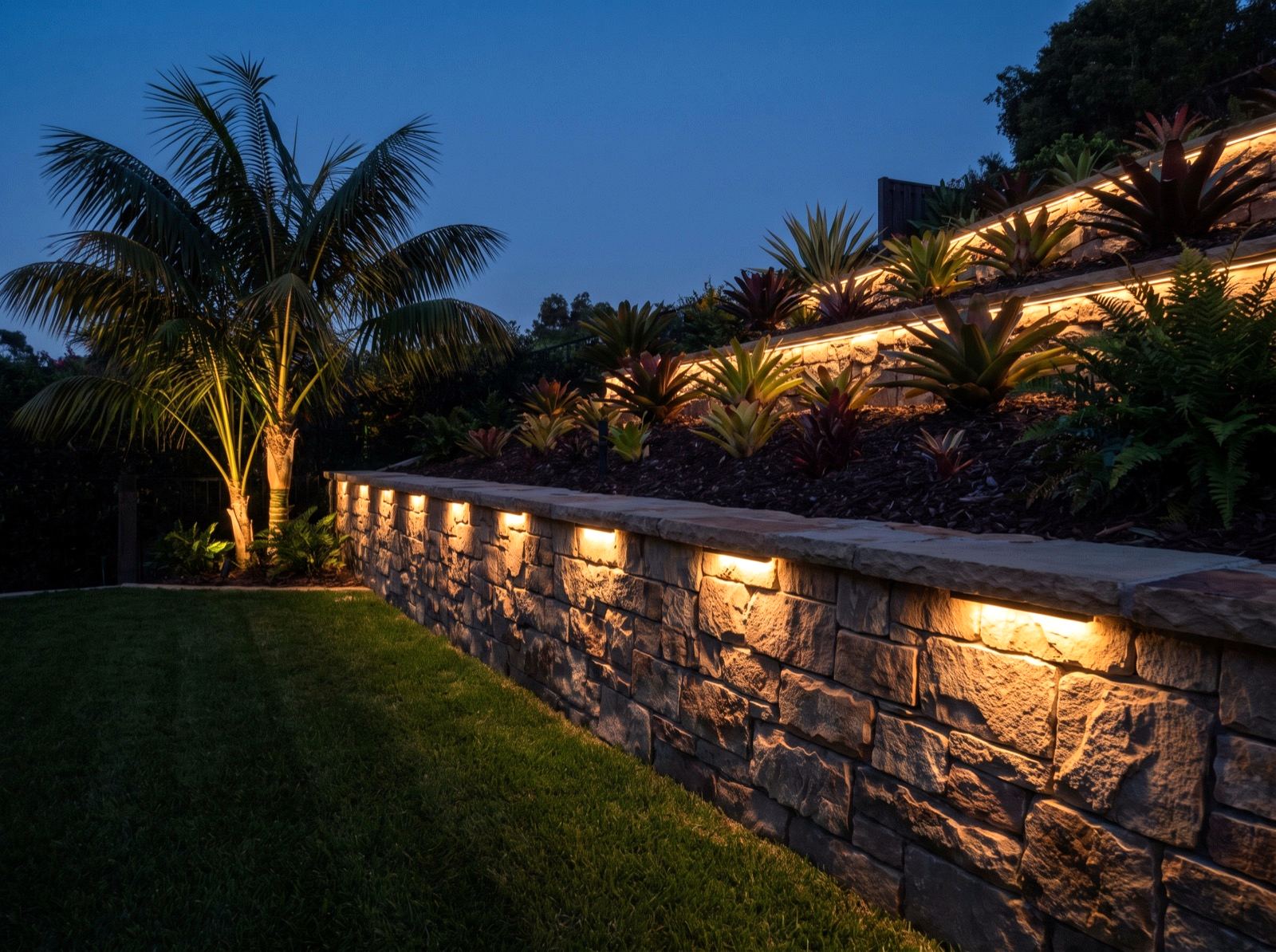 Stacked-stone retaining wall with warm lighting recessed under the cap course